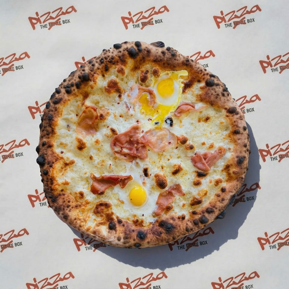 A Pizza The Boxee Box pizza with eggs and bacon on branded paper.