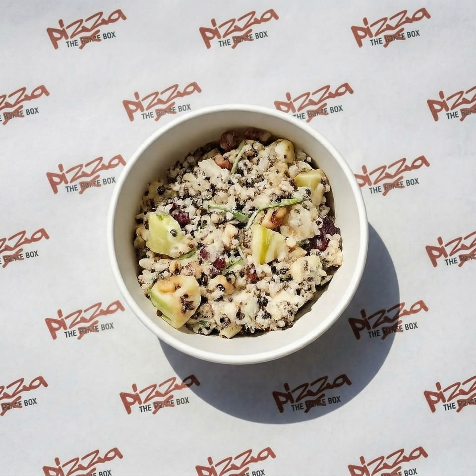 Overhead view of a white bowl filled with a creamy salad containing quinoa, apples, and nuts.