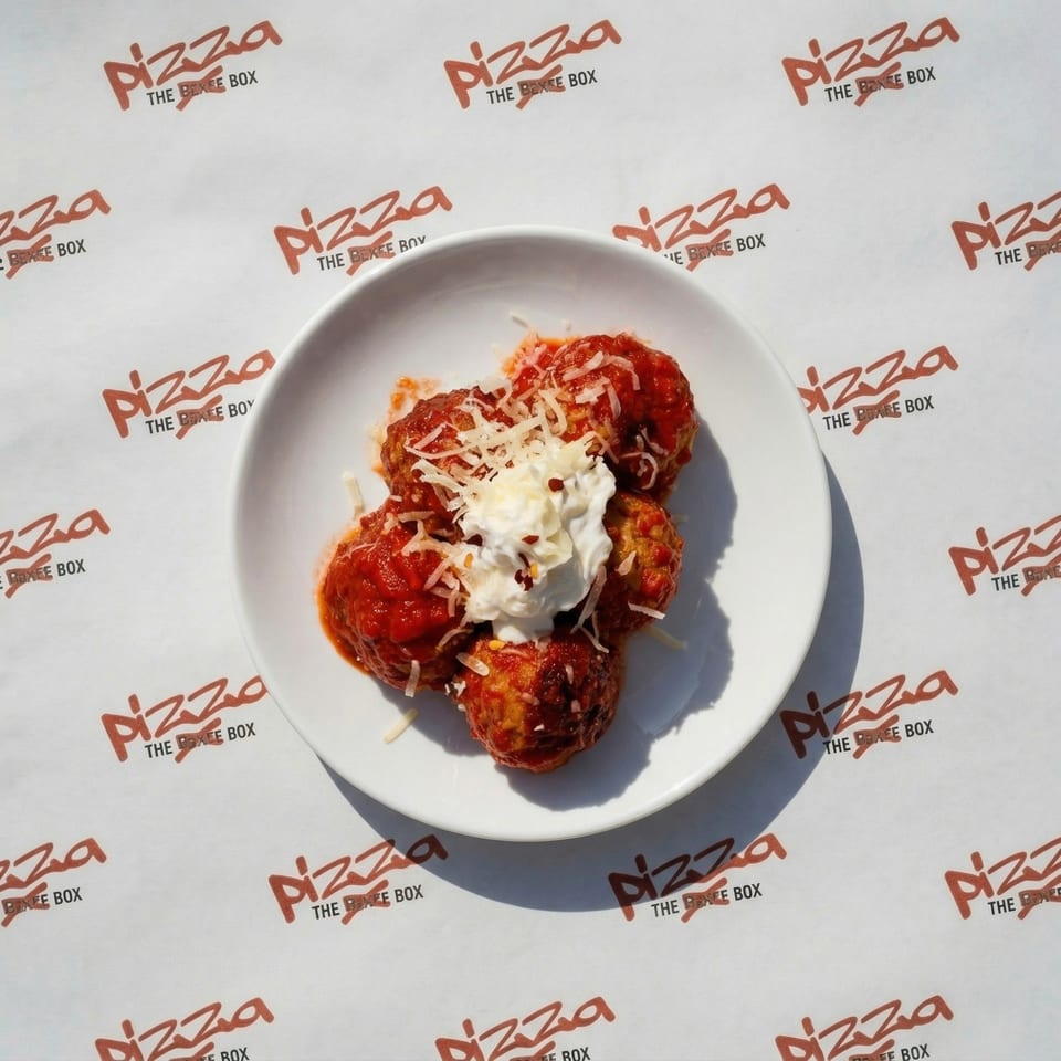 Meatballs in red sauce with a dollop of sour cream and shredded cheese on a white plate.